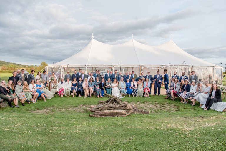 Sailcloth marquee with three poles in the tent. Wedding party of 150 guests in the marquee in Yorkshire. Guests having the group photo outside the marquee structure.