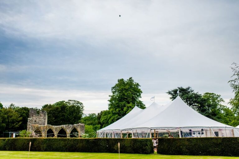 Sailcloth marquee with three poles in the tent. Wedding party of 150 guests in the marquee in Yorkshire. Old ruins next to the pole tent and green hedge