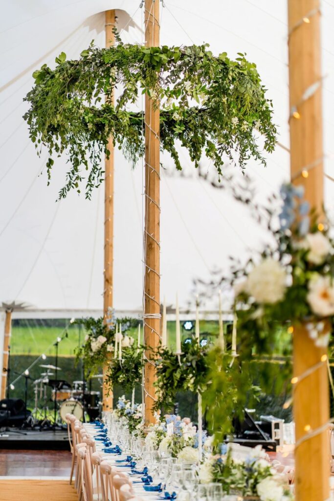 layout inside the pole tent. flower hoops around the poles in the marquee with long tables and chairs set up for a wedding