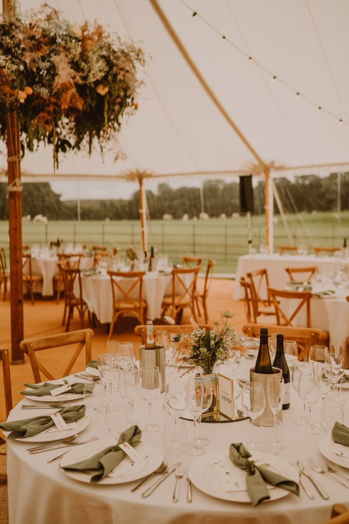 Interior of the sailcloth tent laid up with round tables and chairs for the wedding. Flower hoops around the poles and matted flooring. blush pinks in the flowers.