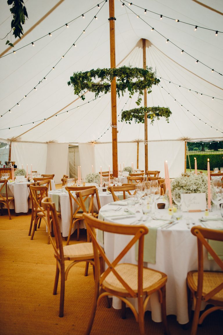 interior of a pole tent. tables and chairs set for a wedding breakfast. fairy lights and flower hoops inside the marquee.