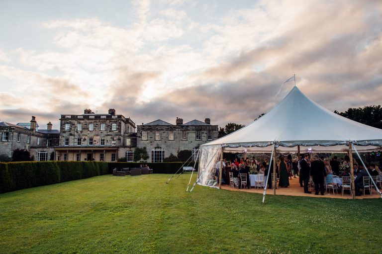 Aurora Sailcloth tent with one pole for a wedding party in the grounds of a stately home in Yorkshire. Sunny day , blue skies, sides rolled up on the marquee.