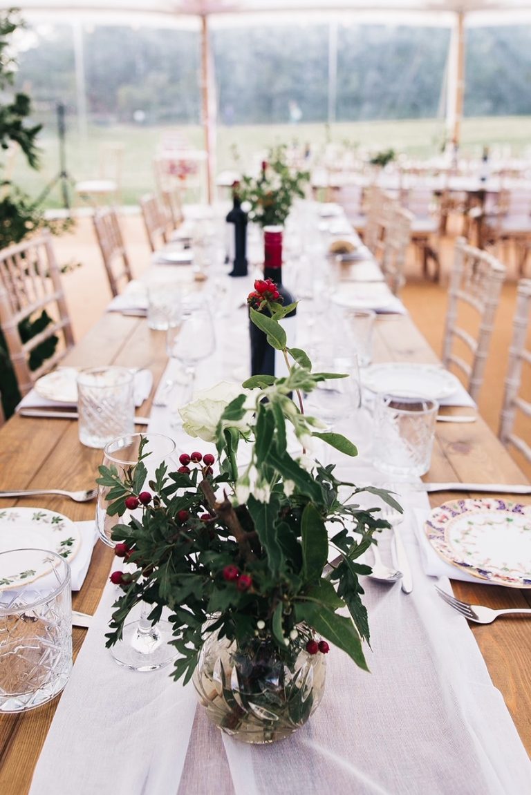 rustic long tables and chairs in the pole tent. flower decorations on the tables and red wine