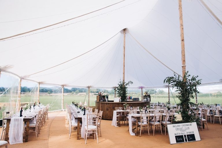 interior of the pole tent at a wedding. Long rustic tables and Chiavari chairs with a circular bar around one of the poles in the tent