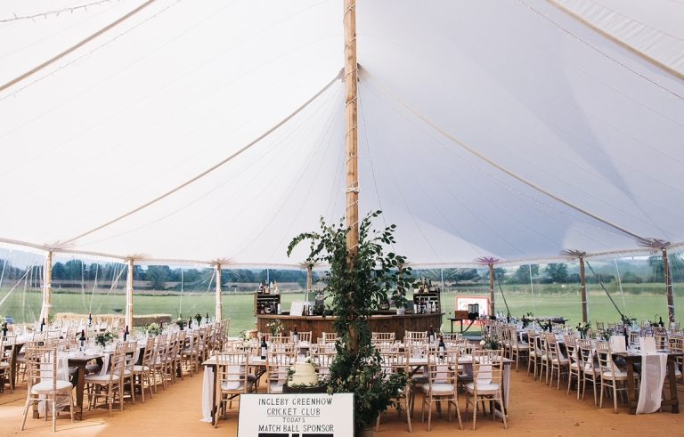 interior of the pole tent at a wedding. Long rustic tables and Chiavari chairs with a circular bar around one of the poles in the tent