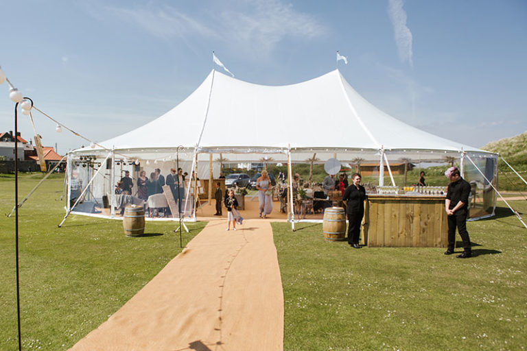 sailcloth marquee with two poles in the tent. matted walkway to the entrance of the marquee. Circular bar at the side of the tent.
