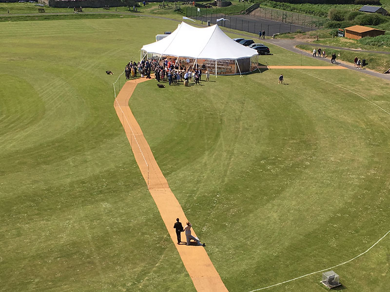 Marquee with two poles and a long matted walkway to the entrance of the tent. In the grounds of Bambrugh Castle for a wedding.