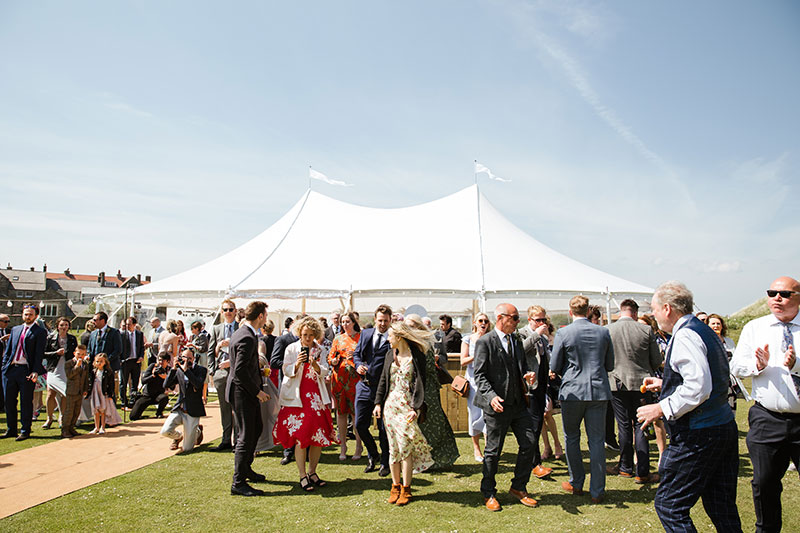 Wedding guests standing outside the sailcloth tent . Marquee has two poles inside and there is 80 guests around the marquee in Yorkshire