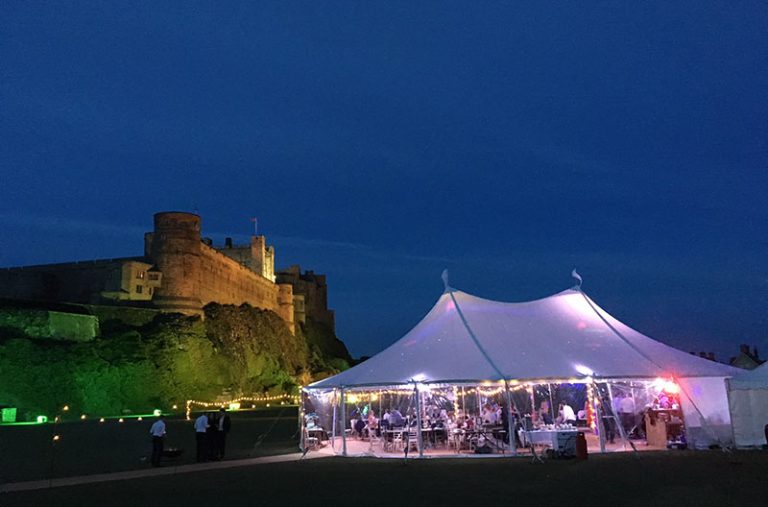 Wedding in the grounds of Bambrugh castle in a Sperry style tent lit up at night time