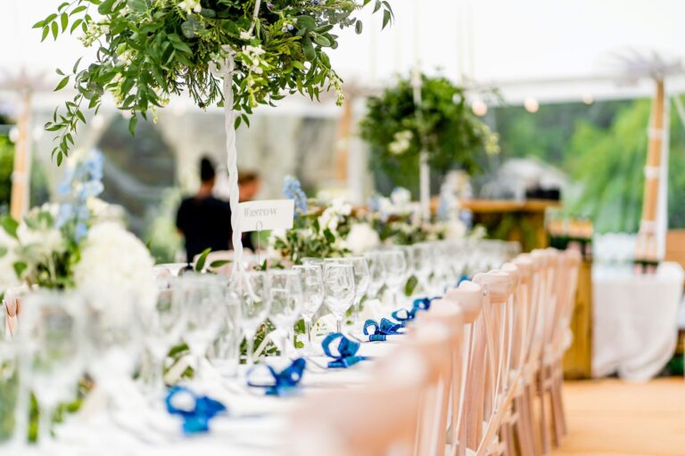 interior of a pole tent with long tables, blue ribbons and flowers set up for a wedding