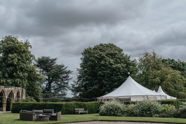 pole tent in the ground of a stately home. marquee is used for a wedding with rattan sofas to relax on
