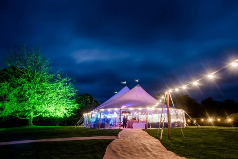 Wedding marquee lit up for a evening party with festoon lights over the top of the tent and up lighters around the marquee.